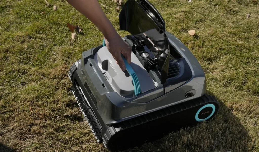 Capot supérieur de l'Aiper Scuba X1 ouvert, une main extrait le panier filtrant par le dessus