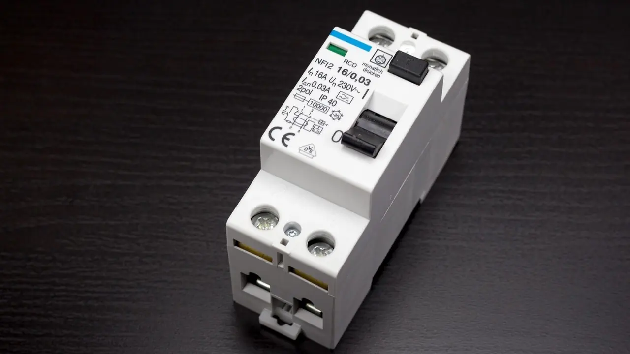 Interrupteur différentiel bipolaire blanc marqué 0,03 A et 230 V, bouton de test noir, posé sur un plan sombre