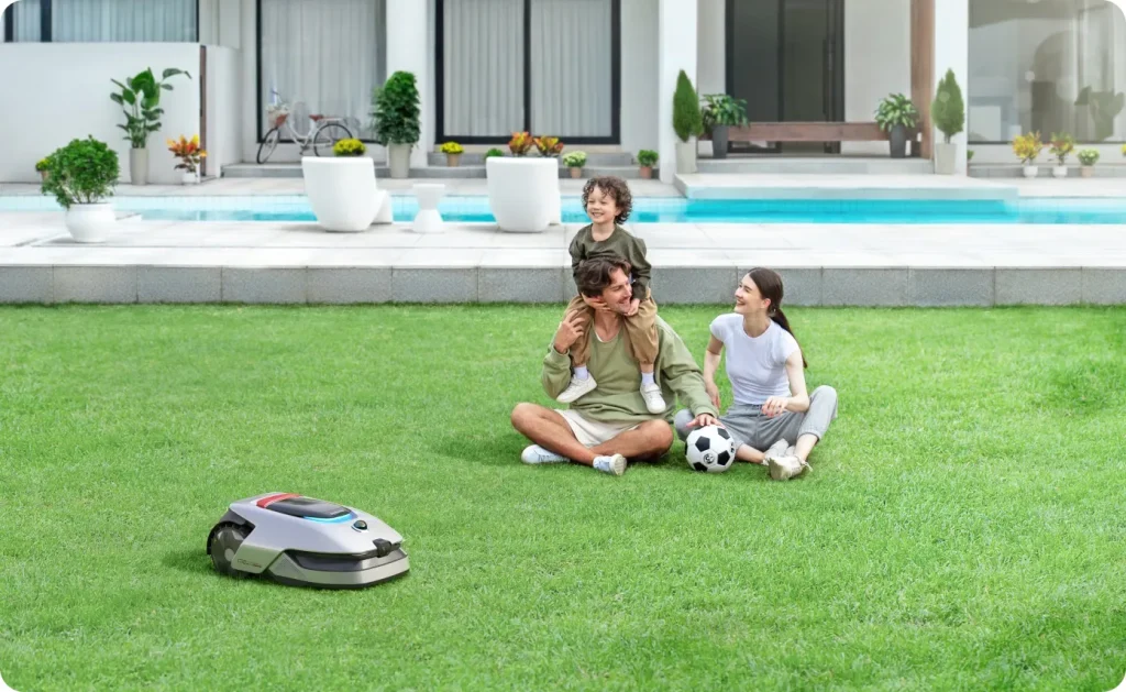 Robot tondeuse Dreame A2 tondant discrètement près d'une famille assise sur la pelouse au bord de la piscine
