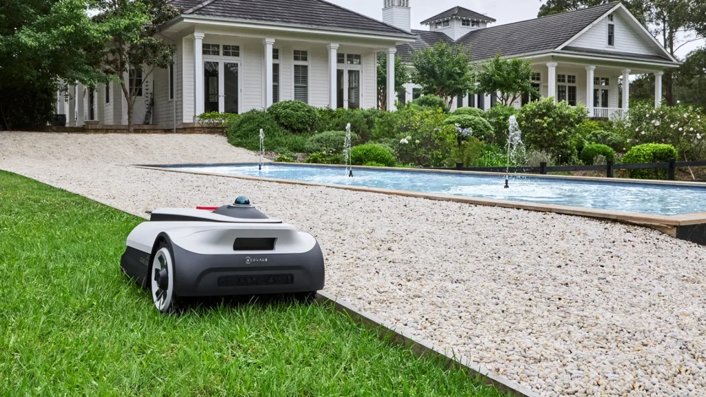 Robot tondeuse Ecovacs Goat A3000 LiDAR tondant le long d'une bordure de gravier au bord d'un bassin dans un grand jardin