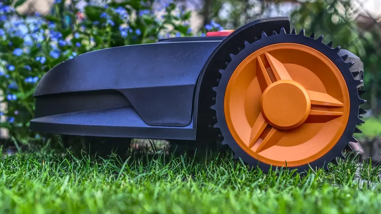 Gros plan d'un robot tondeuse noir à roue crantée orange sur une pelouse verte : faut-il mettre de l'engrais avec un robot tondeuse