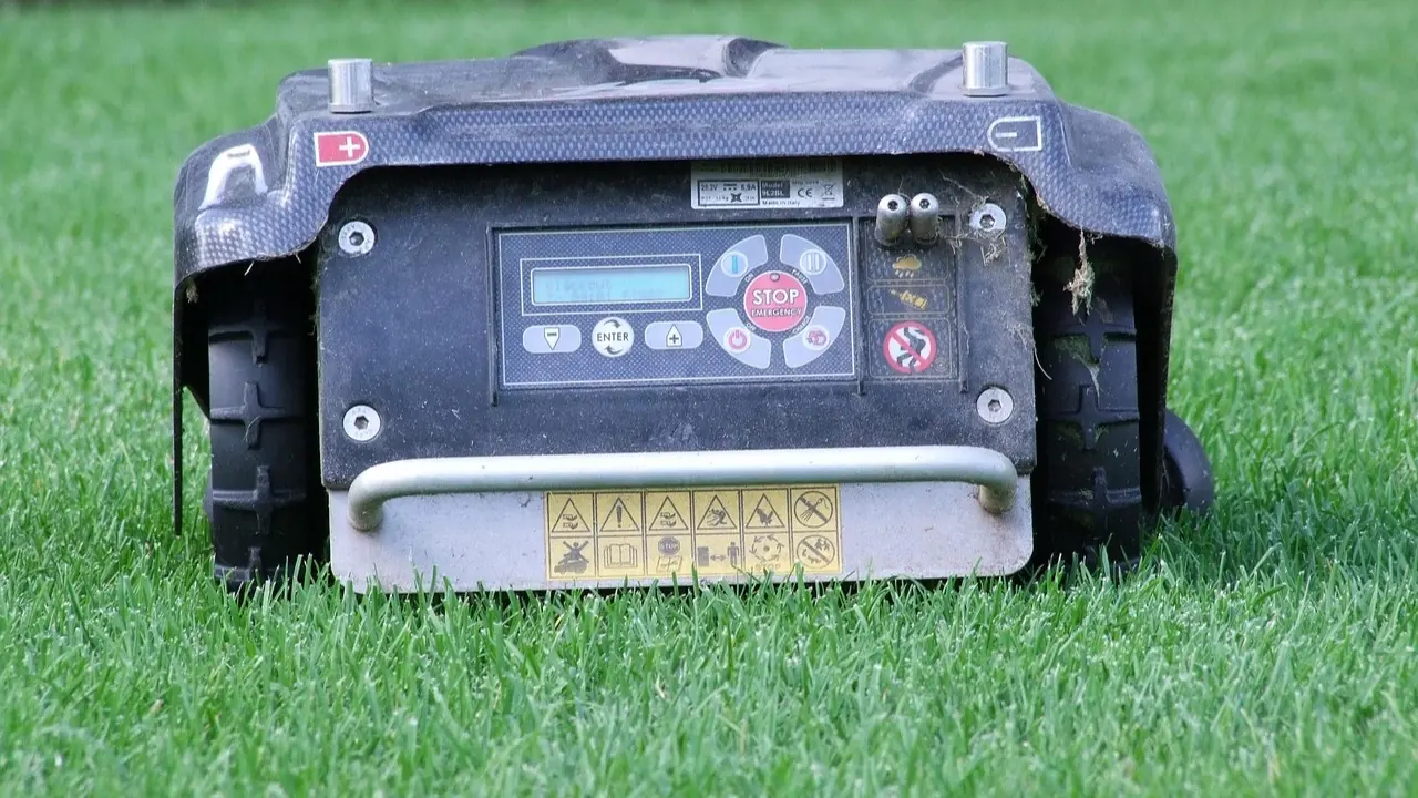 Face arrière d'un robot de tonte posé sur l'herbe, avec son écran d'affichage, son clavier de programmation et son bouton d'arrêt rouge
