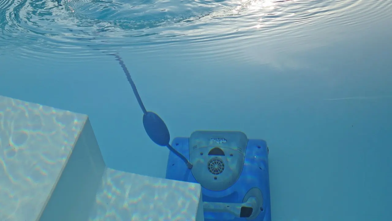 Peut-on se baigner avec le robot de piscine dans l'eau : vue sous-marine d'un robot bleu arrêté au pied des marches blanches d'un bassin, son câble flottant remontant vers la surface