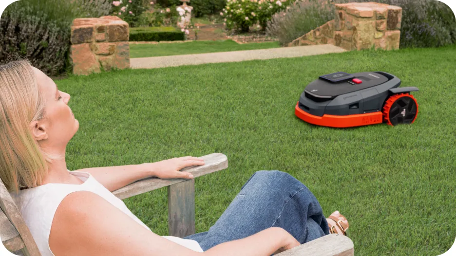 Robot tondeuse Segway Navimow X3 tondant la pelouse pendant qu'une femme se détend dans une chaise de jardin